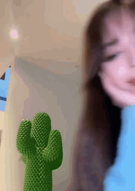 a woman in a blue sweater is standing next to a green cactus statue