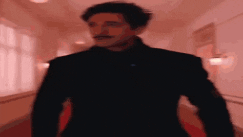 a man with a mustache is walking down a hallway in a black suit .