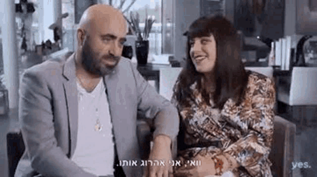 a man and a woman are sitting next to each other in a living room holding hands and smiling .