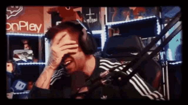 a man wearing headphones is covering his face while sitting in front of a microphone in a room .