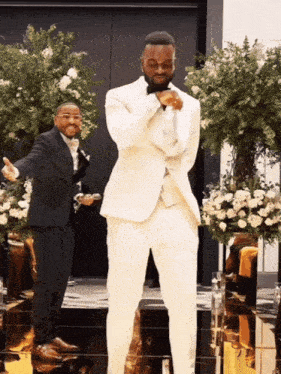 a man in a white suit is standing next to another man in a black suit