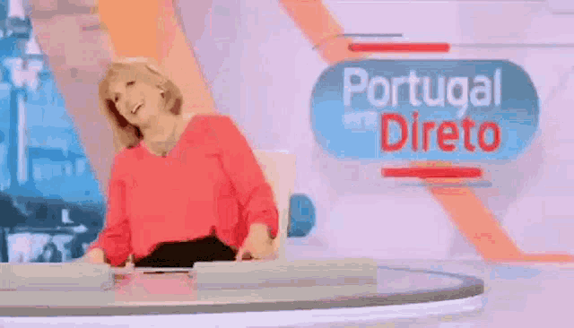 a woman in a red shirt is standing in front of a portugal em direto sign