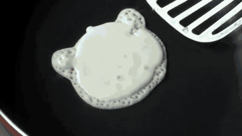 a pancake in the shape of a teddy bear is being cooked in a frying pan