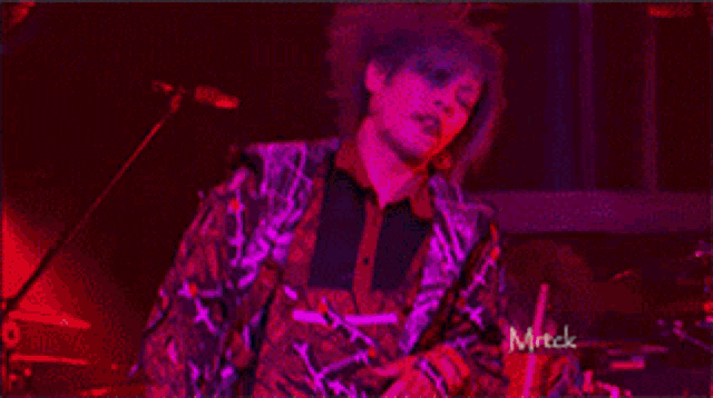 a man with purple hair is singing into a microphone on a stage