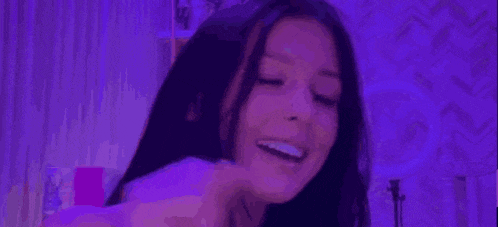 a woman with long black hair is standing in front of a purple light .