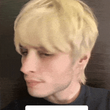 a man with blonde hair and a beard is wearing a black shirt and looking at the camera .