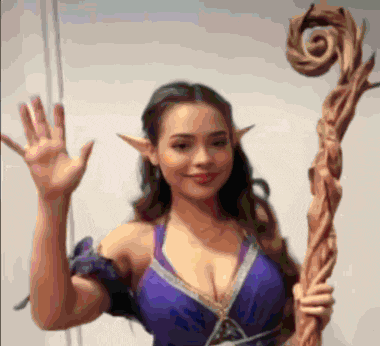 a woman in a purple dress with elf ears holds a wooden cane