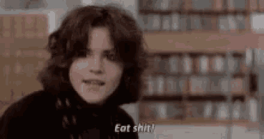 a woman is standing in front of a bookshelf in a library and says `` eat shit '' .