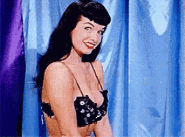 a woman in a black bra is smiling in front of blue curtains
