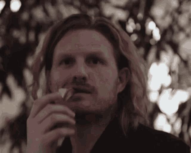 a man with long hair and a beard is eating a piece of cheese