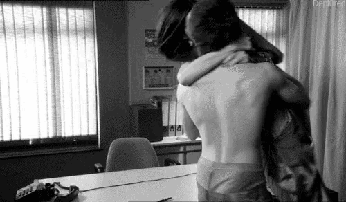 a black and white photo of a man and woman hugging each other in an office .