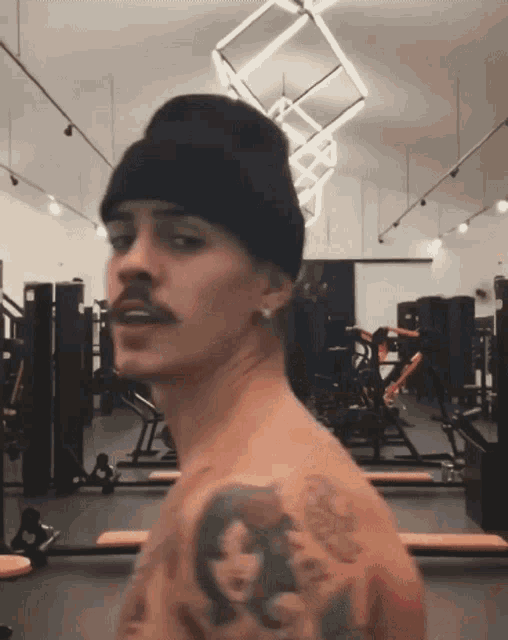 a man with a mustache wearing a black beanie and earrings is in a gym