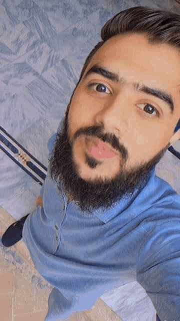 a man with a beard is taking a selfie while wearing a blue shirt .