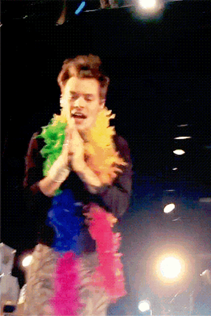 a man wearing a rainbow colored feather boa stands on a stage