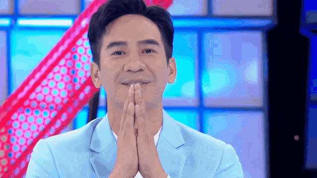 a man in a blue suit is holding his hands together in front of his face .