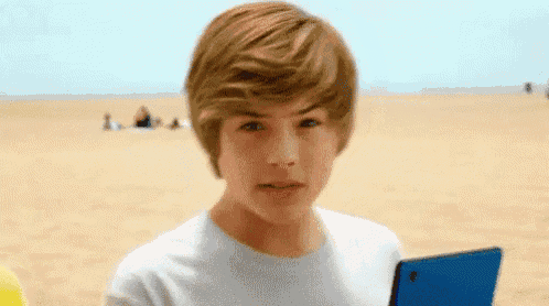 a young boy is holding a tablet on the beach and looking at the camera .