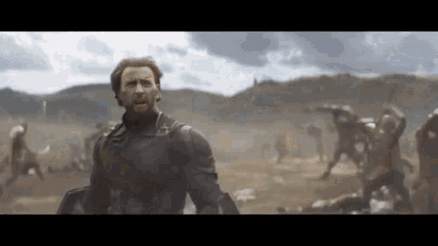 a man in a superhero costume is standing in a field with a group of people in the background .