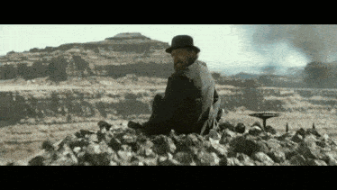 a man in a top hat sits on a pile of rocks in the desert