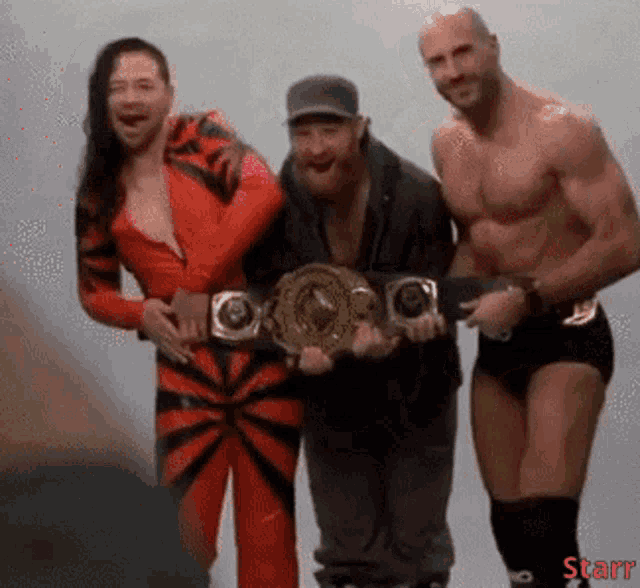 three wrestlers are posing for a picture and one of them is holding a championship belt