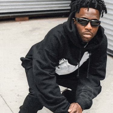 a man wearing sunglasses and a black hoodie with a white bird on it