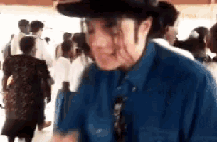 a man wearing a hat and a blue shirt is standing in front of a crowd of people
