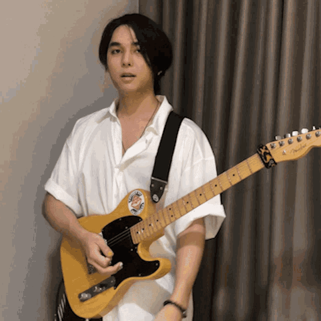 a man in a white shirt is holding a guitar with a fender sticker on it