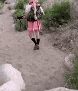 a woman in a pink skirt is walking down a dirt road holding a gun .