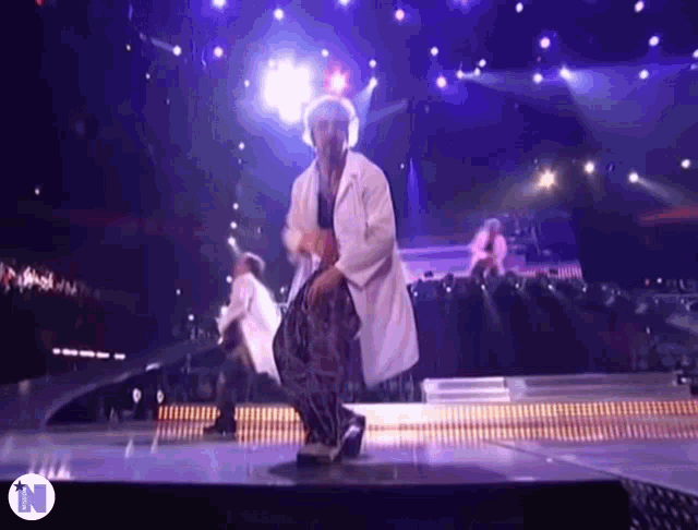 a man in a white coat is dancing on a stage with the letter n in the corner