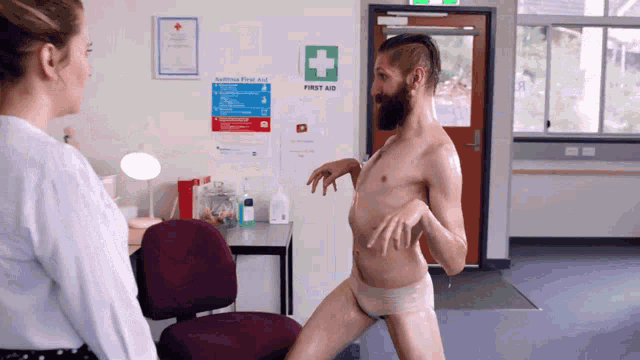 a man without a shirt is dancing in front of a first aid sign