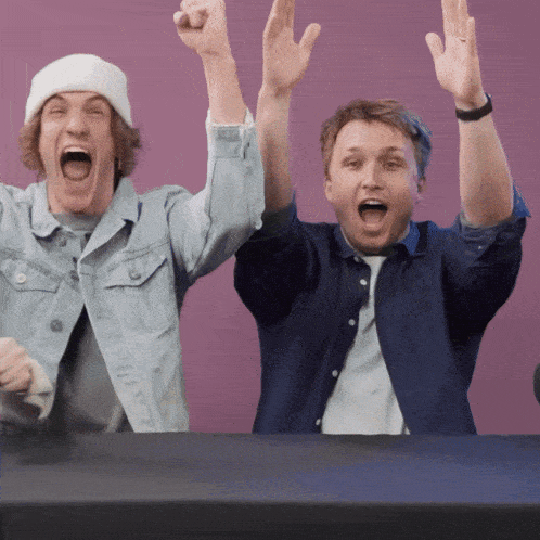 two men are raising their arms in the air and one is wearing a beanie