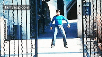 a man in a blue shirt and jeans is standing in front of a fence .
