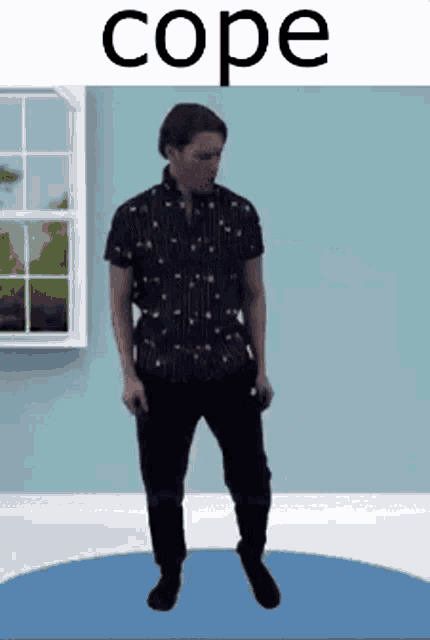 a man in a black shirt and black pants is standing on a blue circle in a room .
