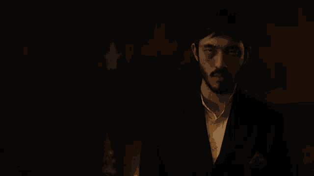 a man with a beard is standing in a dark room in a suit .