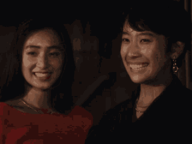 two women holding hands and smiling at each other in a dark room