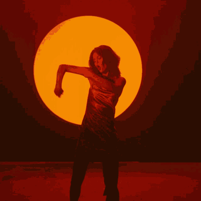 a woman in a black dress is dancing in front of a large orange sun