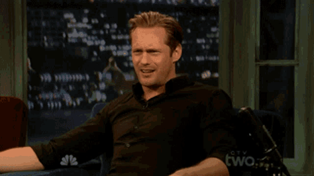 a man in a black shirt sits on a couch in front of a screen that says two