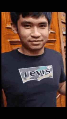 a man wearing a levis t-shirt is standing in front of a wooden door