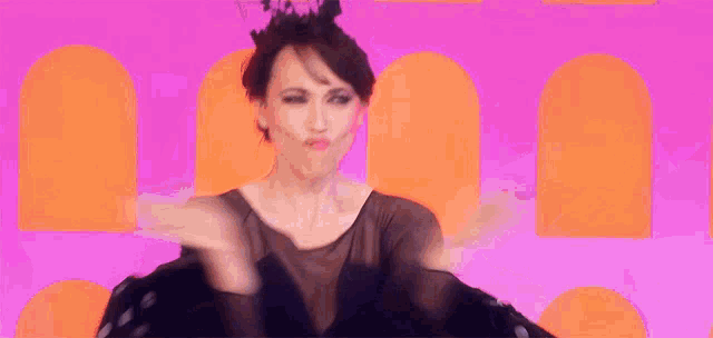 a woman wearing a black crown is dancing in front of a pink and orange background