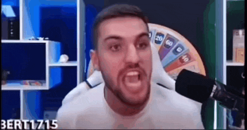 a man with a beard is screaming into a microphone in front of a spinning wheel .