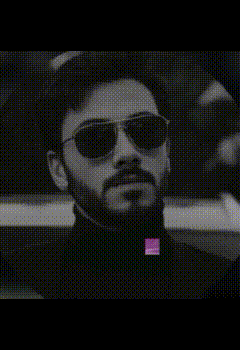 a man with a beard wearing sunglasses and a black turtleneck holds a purple object in his mouth .