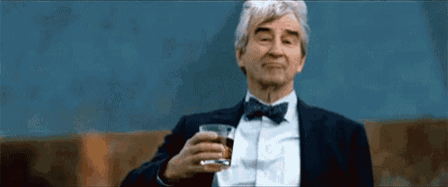 an older man in a suit and bow tie is holding a glass of whiskey
