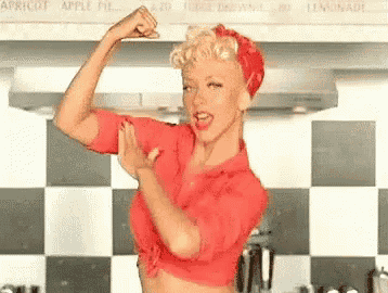 a woman is flexing her muscles in a kitchen while wearing a red shirt and a red headband .