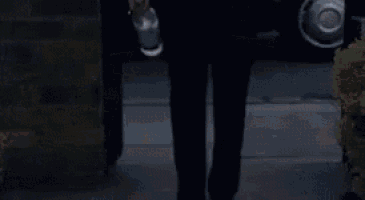 a woman in a white jacket and black pants is walking in front of a black car .