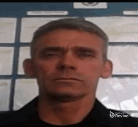 a man with a serious look on his face is standing in front of a wall of papers .