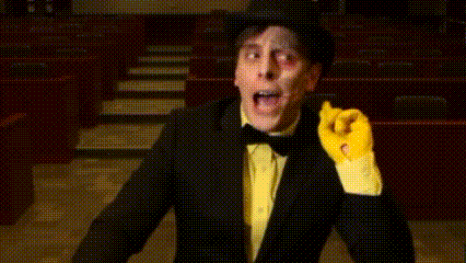 a man in a tuxedo and yellow gloves is standing in front of an auditorium .