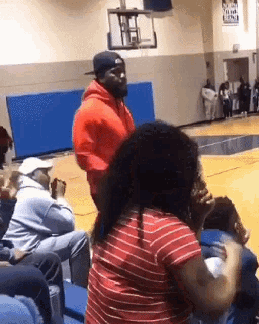 a man in a red hoodie is standing next to a woman in a red striped shirt on a basketball court .