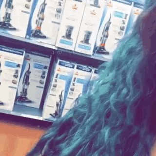 a woman with blue hair is standing in front of a shelf of vacuum cleaners .