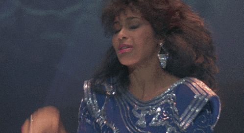 a woman in a blue sequined top is dancing in front of a pink background