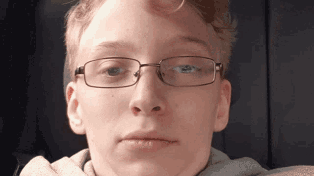 a young man wearing glasses and a grey hoodie looks at the camera