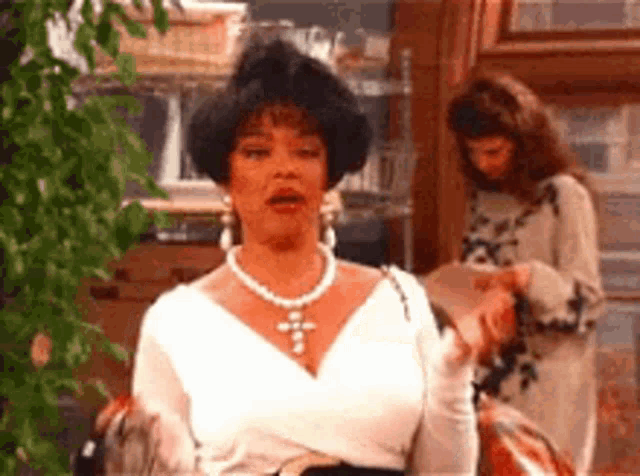 a woman wearing a white top and a pearl necklace is sitting in a chair .